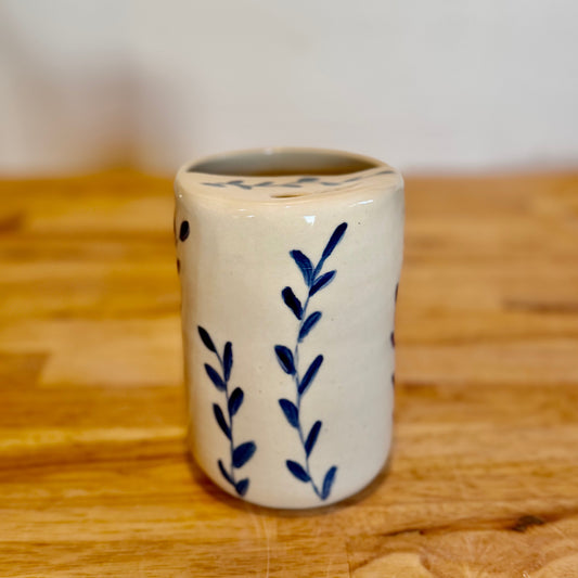 White ceramic cup with blue leaf patterns on a wooden surface