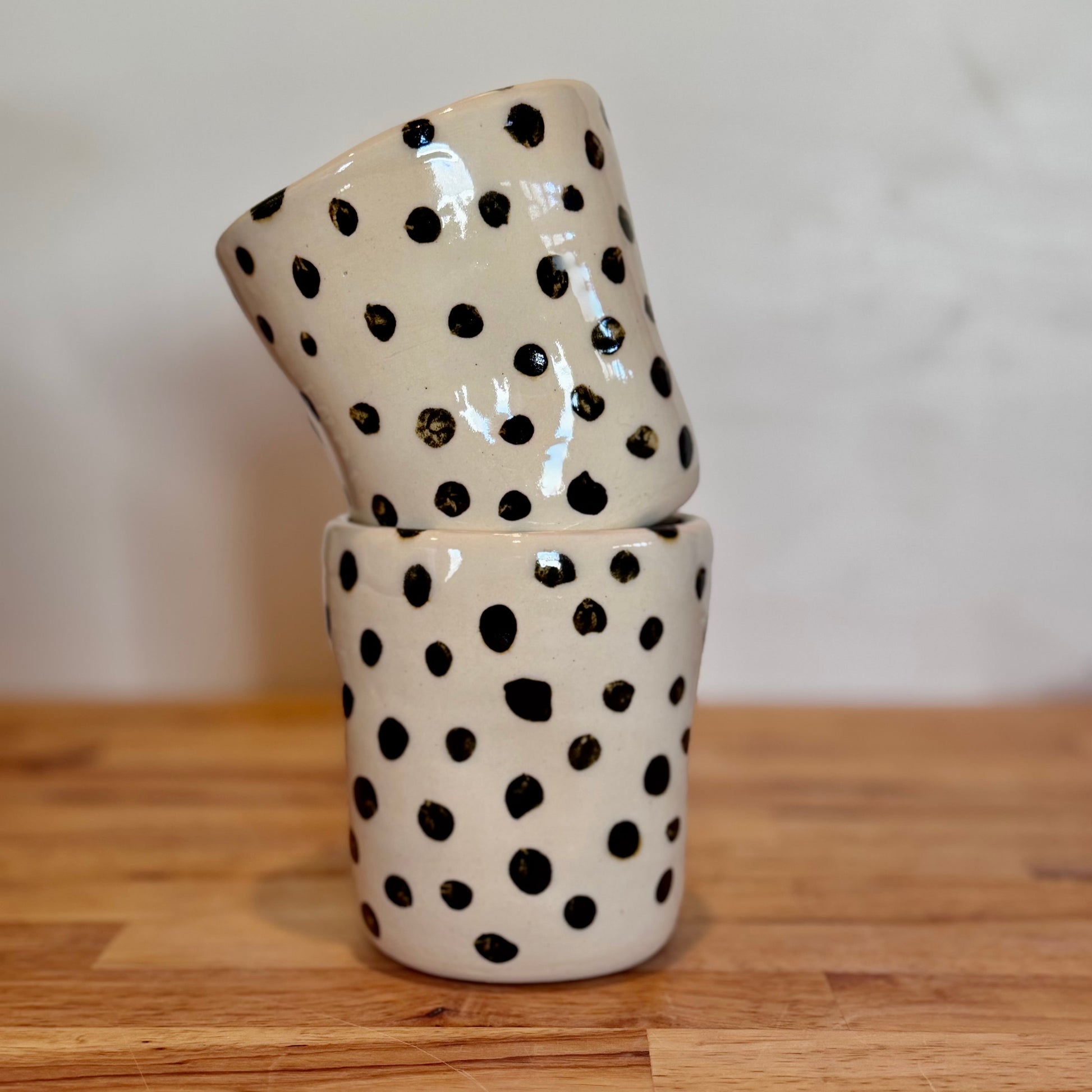 Two ceramic cups with black polka dots stacked on a wooden surface.