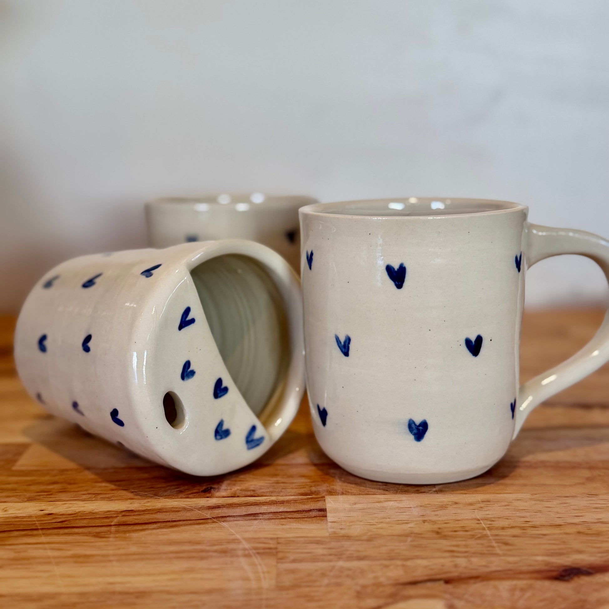 Two ceramic mugs with blue heart patterns on a wooden surface.