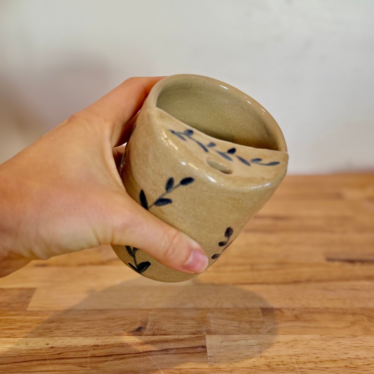 Hand holding a ceramic cup with blue floral designs on a wooden surface