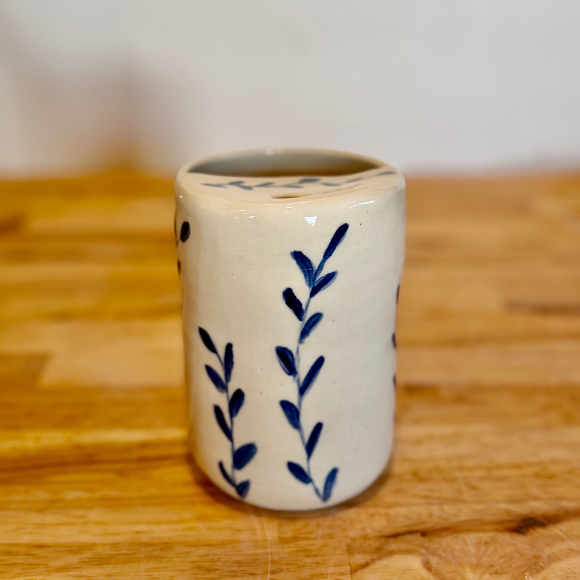White ceramic cup with blue leaf patterns on a wooden surface
