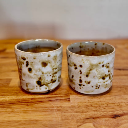 Two ceramic cups with speckled design on a wooden surface